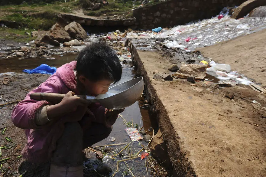 A child drinks water near a stream in Fuyuan county